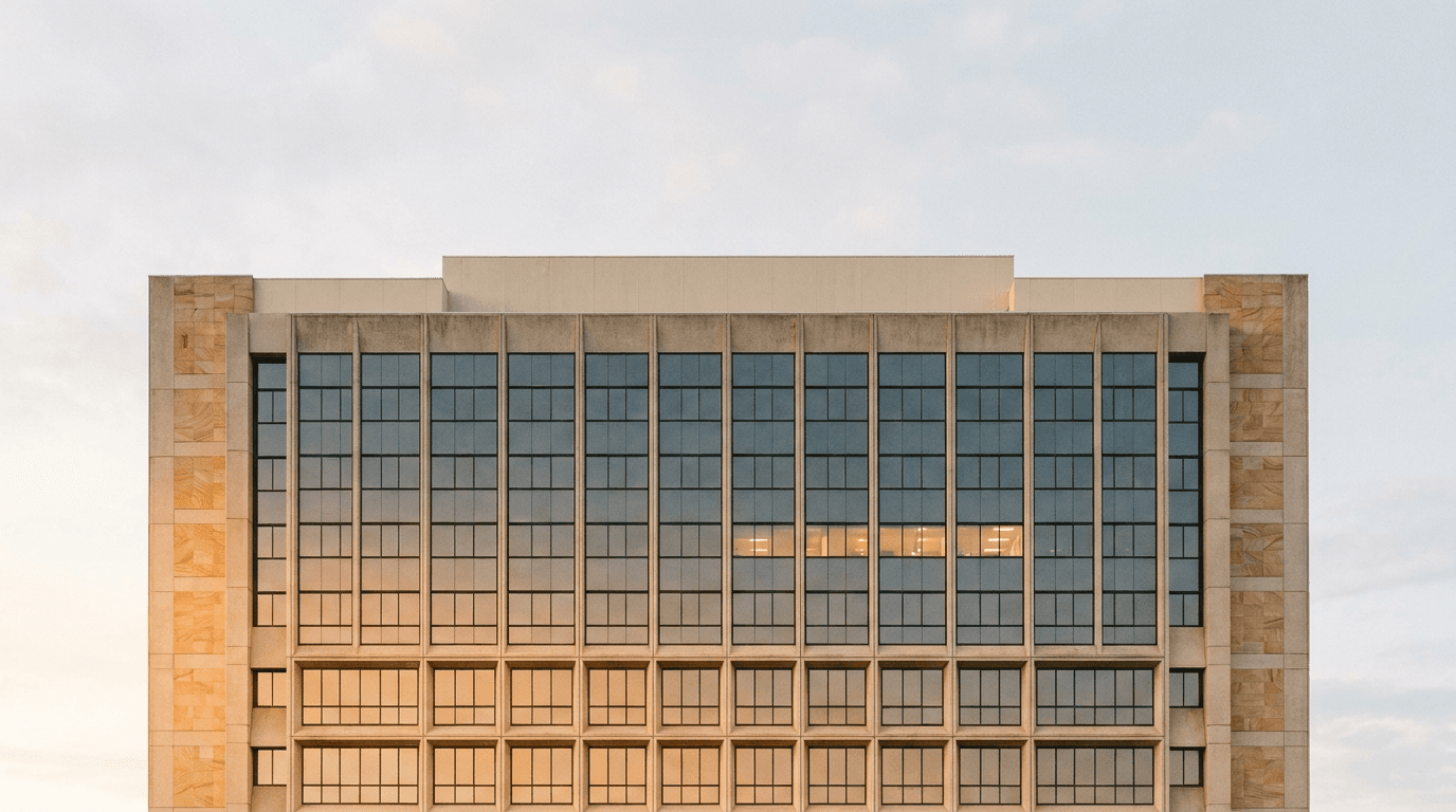 Facade of an Australian commercial building, its grid of identical windows lit in a gradient from warm amber to cool slate — an orderly ledger of glass